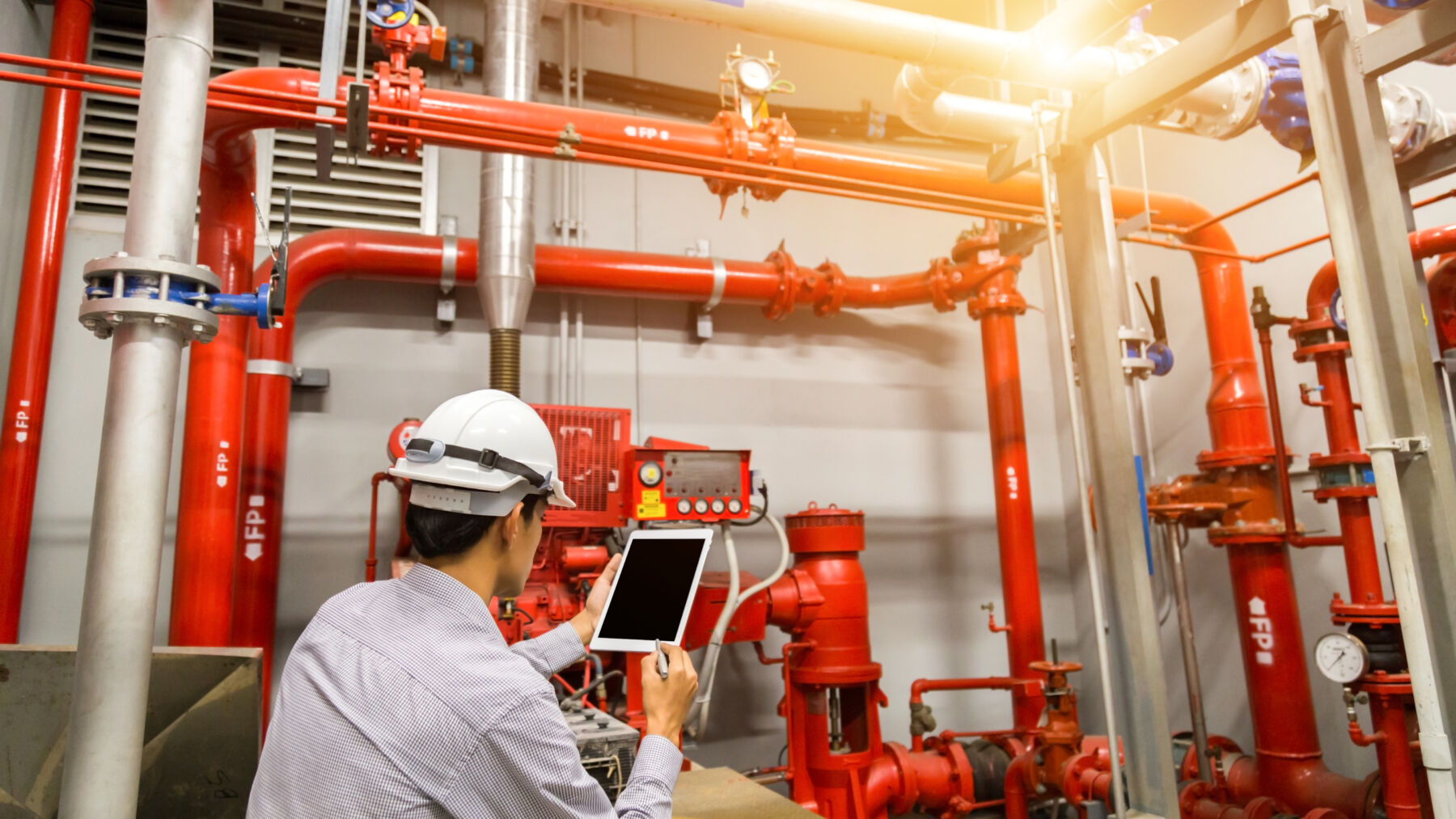 Engineer with tablet check red generator pump for water sprinkler piping and fire alarm control system.